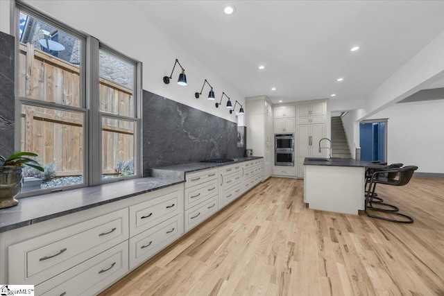 kitchen featuring dark countertops, light wood-style flooring, decorative backsplash, and a kitchen bar