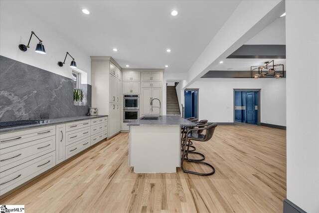 kitchen featuring a sink, stainless steel double oven, light wood finished floors, and gas cooktop