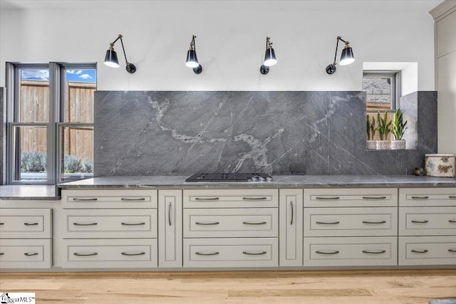 kitchen with light wood finished floors, stainless steel gas cooktop, decorative backsplash, and dark stone counters