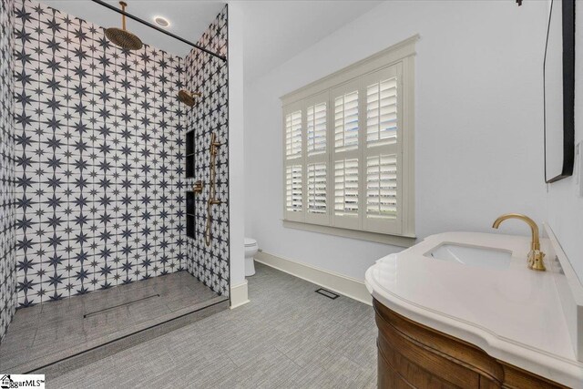 full bathroom featuring visible vents, baseboards, toilet, a tile shower, and vanity