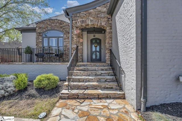 view of exterior entry with fence and brick siding