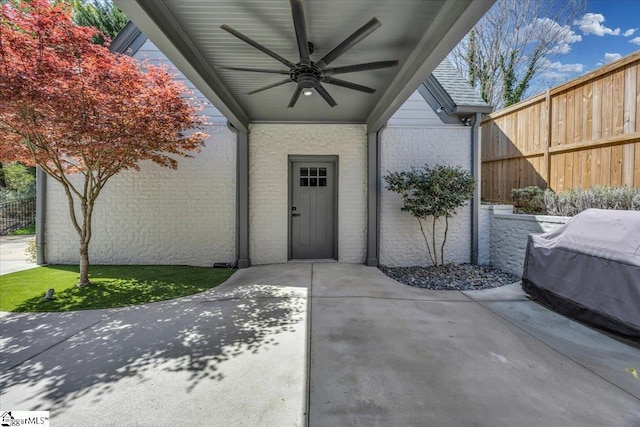 doorway to property featuring a ceiling fan, brick siding, fence, and a patio