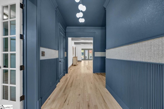 hall with a wainscoted wall, ornamental molding, and light wood-style flooring