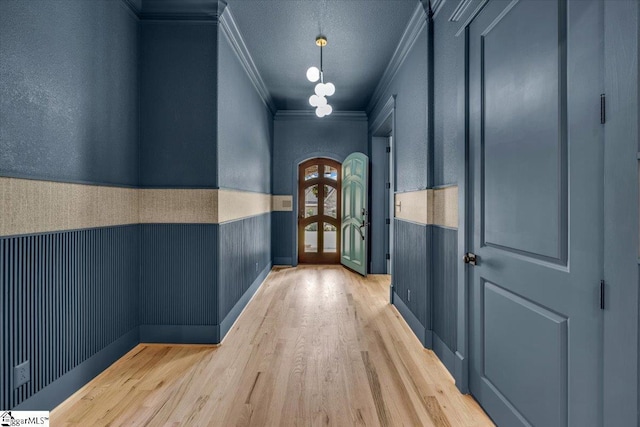 corridor with wainscoting, wood finished floors, ornamental molding, and french doors
