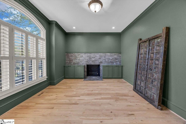 unfurnished living room featuring ornamental molding, baseboards, a stone fireplace, and wood finished floors