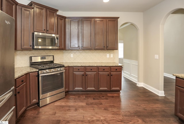 kitchen featuring arched walkways, stainless steel appliances, dark wood-type flooring, and tasteful backsplash