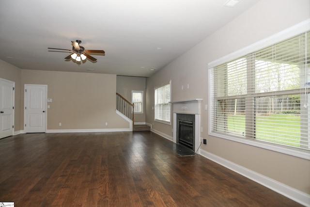 unfurnished living room featuring stairway, a premium fireplace, baseboards, dark wood-style floors, and ceiling fan