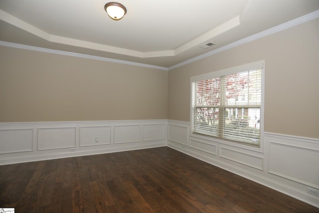 empty room with dark wood-type flooring, visible vents, wainscoting, and a raised ceiling