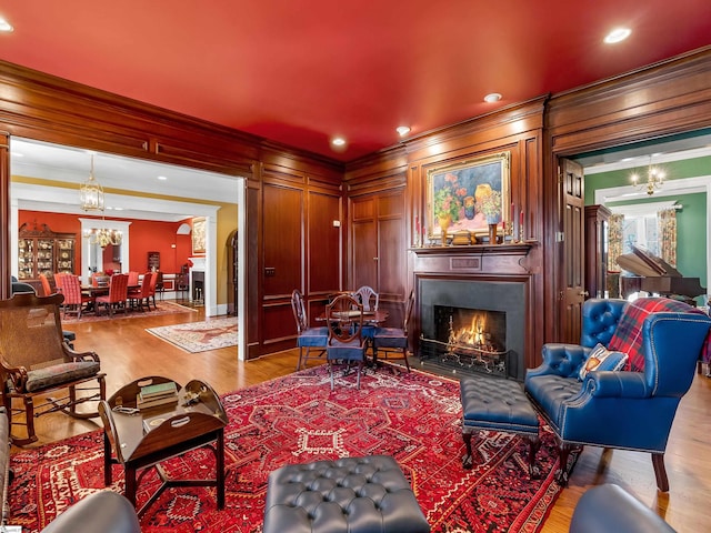 living area with ornamental molding, a notable chandelier, a fireplace with flush hearth, and wood finished floors