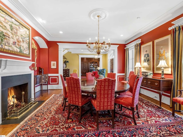 dining room with ornamental molding, wood finished floors, recessed lighting, a lit fireplace, and an inviting chandelier