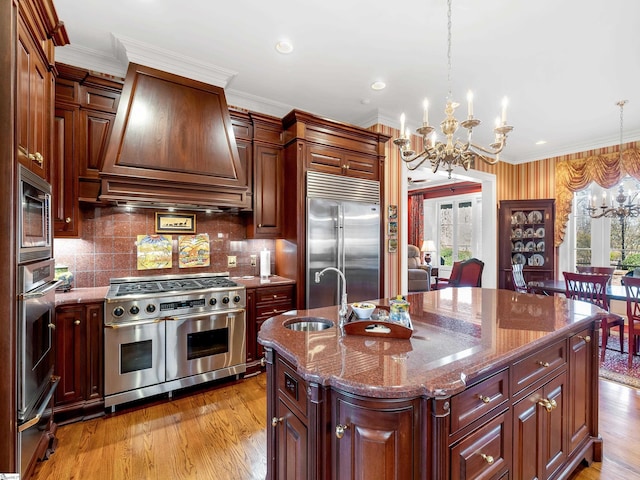 kitchen with a sink, range hood, a chandelier, built in appliances, and plenty of natural light