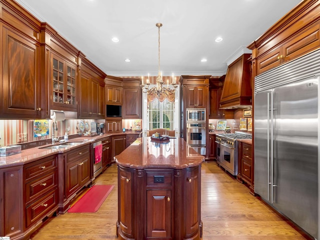 kitchen with light wood finished floors, an inviting chandelier, a sink, custom range hood, and built in appliances