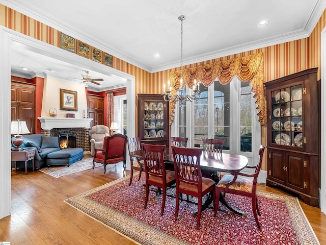 dining room featuring wallpapered walls, crown molding, a fireplace, and wood finished floors