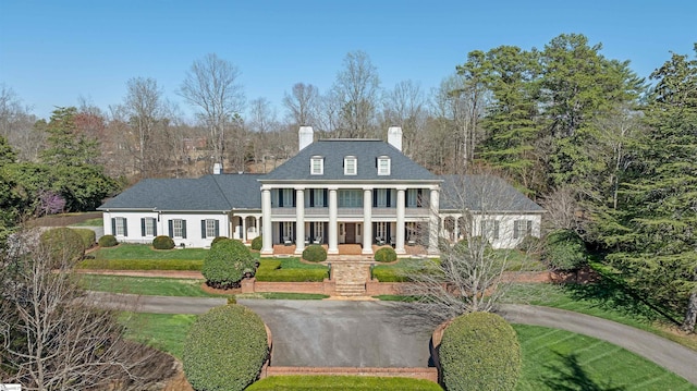 greek revival house with a front lawn, a balcony, and a chimney