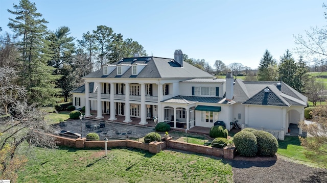 back of property featuring a chimney, a standing seam roof, metal roof, and a yard