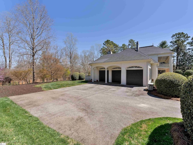 view of side of property featuring central air condition unit, a chimney, an attached garage, stucco siding, and driveway