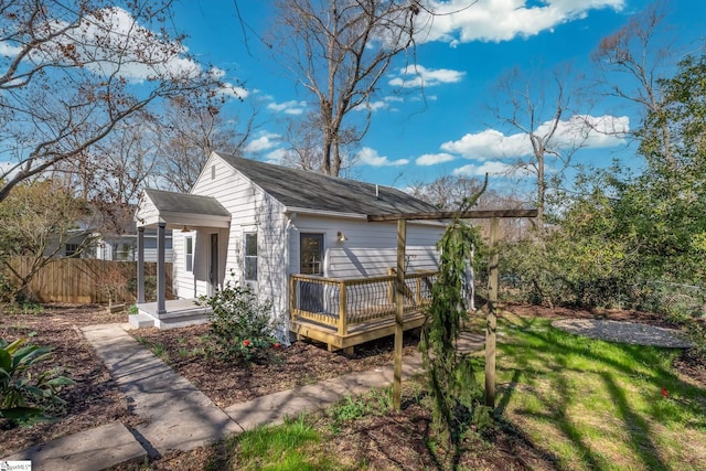 back of property featuring fence, a shingled roof, a yard, and a deck