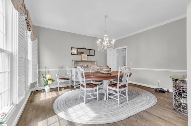 dining space with baseboards, wood finished floors, ornamental molding, and a chandelier