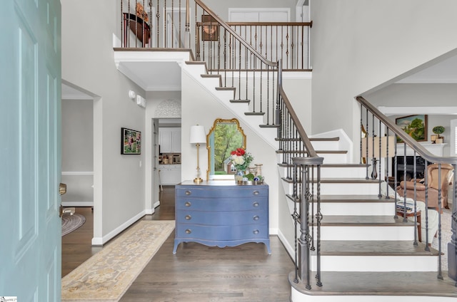 staircase featuring crown molding, baseboards, a high ceiling, and wood finished floors