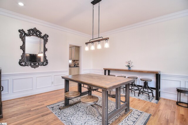 dining space with a wainscoted wall, light wood-style flooring, and ornamental molding