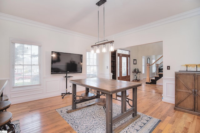 dining space featuring a decorative wall, ornamental molding, stairway, light wood-style floors, and wainscoting