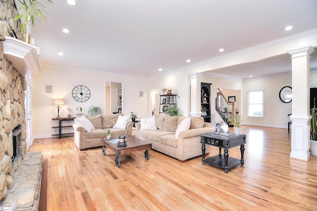 living area with stairway, light wood-type flooring, ornate columns, baseboards, and a stone fireplace