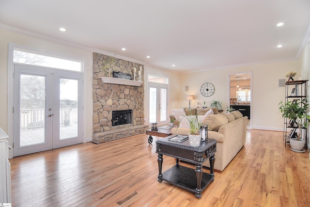 living room featuring ornamental molding, french doors, light wood-type flooring, and a stone fireplace