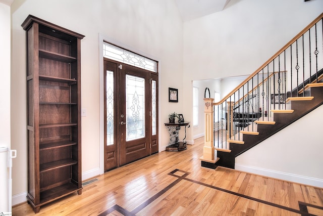 entrance foyer with visible vents, baseboards, stairs, wood finished floors, and a high ceiling
