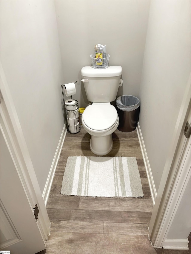 bathroom featuring baseboards, wood finished floors, and toilet