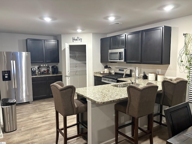 kitchen with a peninsula, light stone countertops, a kitchen bar, appliances with stainless steel finishes, and a sink