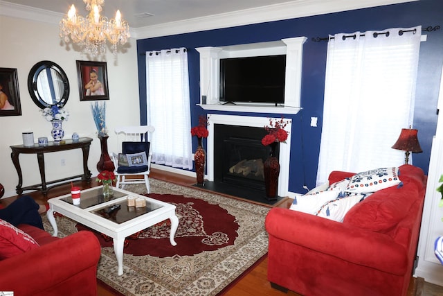 living area with crown molding, a fireplace with raised hearth, a notable chandelier, and wood finished floors