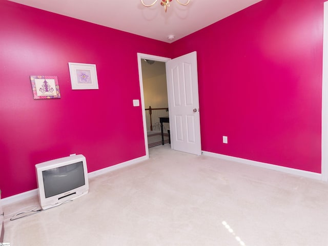 carpeted empty room featuring an inviting chandelier and baseboards