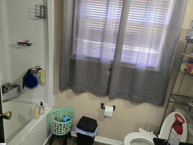 bathroom with toilet, a bathing tub, and baseboards