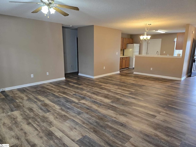 unfurnished living room featuring ceiling fan with notable chandelier, a textured ceiling, baseboards, and dark wood-style floors
