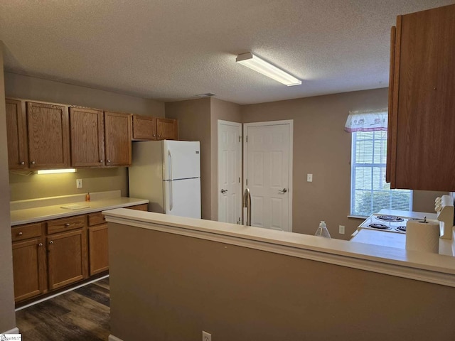 kitchen with dark wood-style flooring, a textured ceiling, light countertops, brown cabinets, and freestanding refrigerator