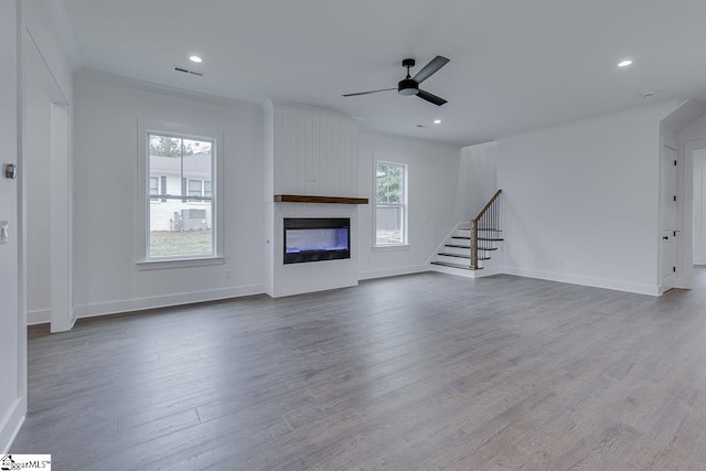 unfurnished living room featuring plenty of natural light, ceiling fan, stairs, and wood finished floors