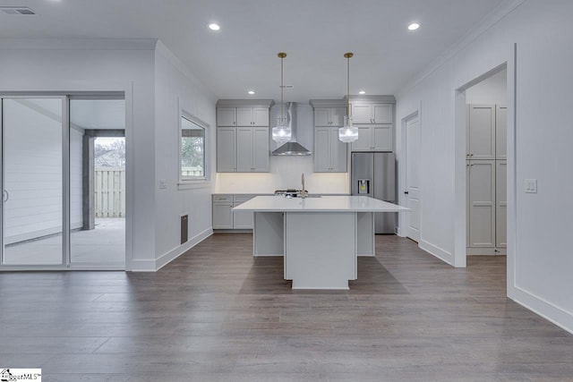 kitchen featuring an island with sink, wall chimney range hood, visible vents, stainless steel refrigerator with ice dispenser, and light countertops