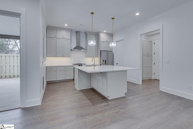kitchen featuring stainless steel refrigerator with ice dispenser, wall chimney exhaust hood, light countertops, light wood-style floors, and a center island with sink