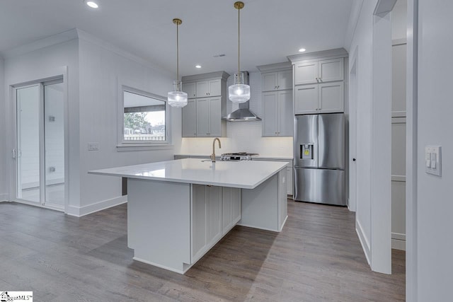 kitchen featuring stainless steel fridge, wall chimney exhaust hood, dark wood-style flooring, light countertops, and a kitchen island with sink