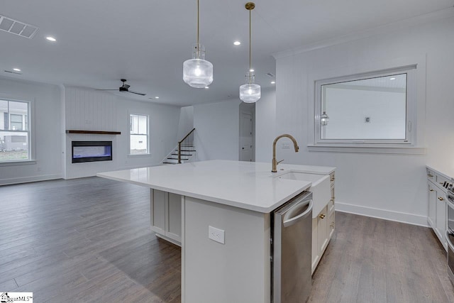 kitchen with stainless steel dishwasher, visible vents, dark wood-style flooring, a sink, and a center island with sink