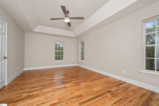 unfurnished room featuring a tray ceiling, ceiling fan, light wood finished floors, and baseboards