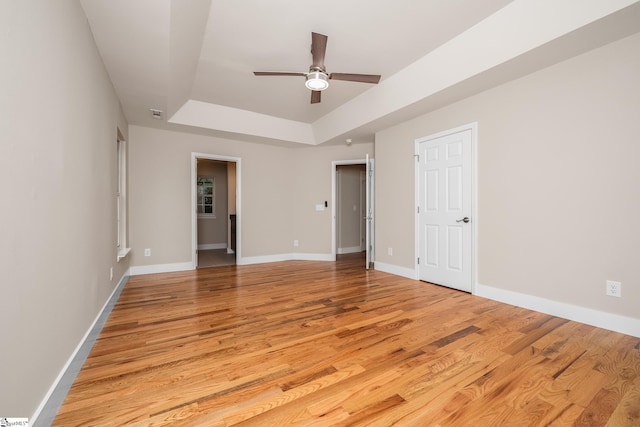 empty room featuring light wood-style flooring, ceiling fan, a raised ceiling, and baseboards
