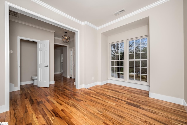 spare room featuring crown molding, visible vents, baseboards, and wood finished floors
