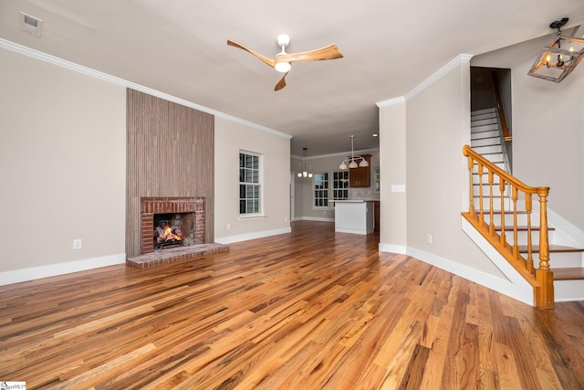 unfurnished living room featuring stairway, light wood-style flooring, a ceiling fan, crown molding, and a brick fireplace