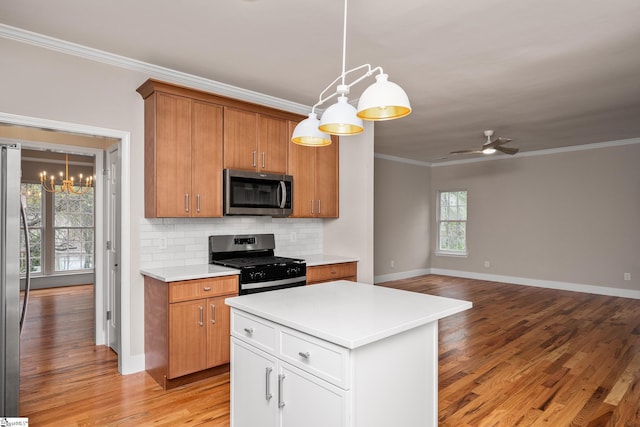 kitchen with light wood-style flooring, light countertops, crown molding, decorative backsplash, and stainless steel appliances