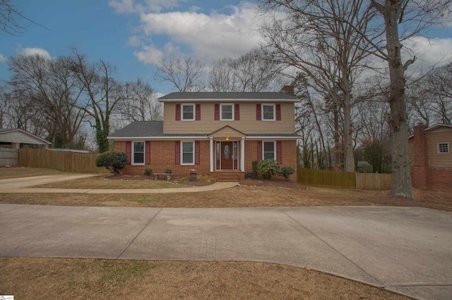 traditional-style home with a chimney, driveway, fence, and brick siding