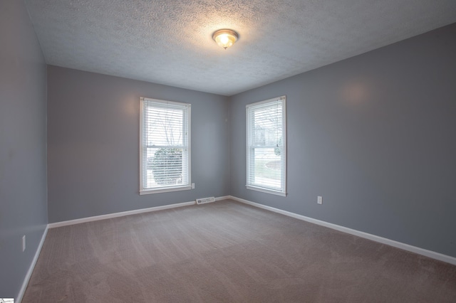 carpeted empty room with visible vents, baseboards, and a textured ceiling