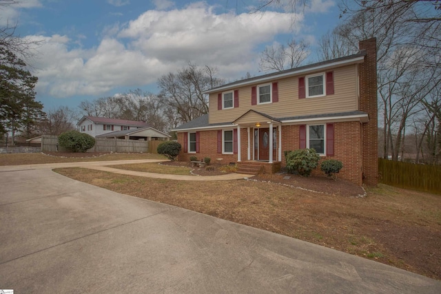 view of front facade with a chimney, driveway, fence, and brick siding
