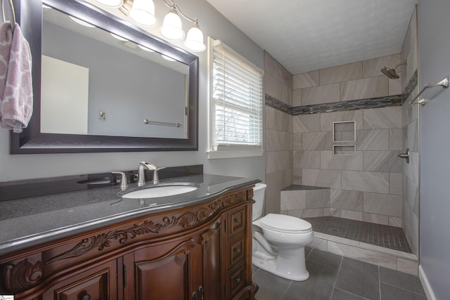 bathroom featuring tile patterned flooring, toilet, tiled shower, and vanity