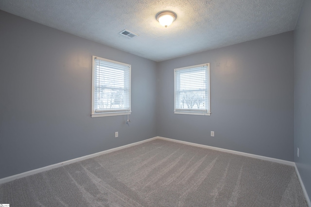 spare room with a textured ceiling, baseboards, carpet, and visible vents